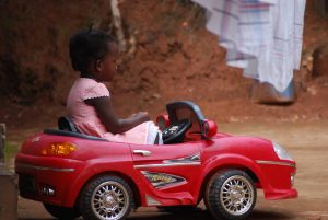 Red Kids Power Wheels with a little child in a pink dress. One of the girls riding a electric powered car bought from an online store.