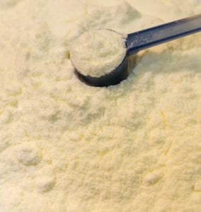 A close-up of a blue scoop measuring powdered infant formula.