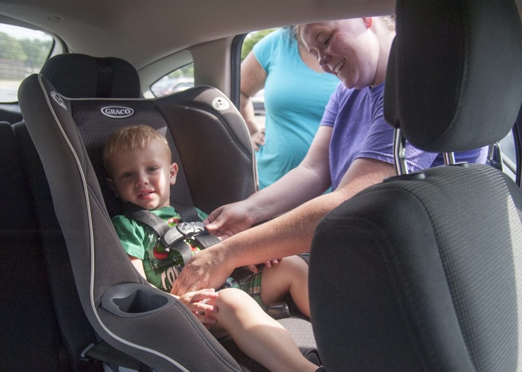 A child getting strapped into a Graco car seat.