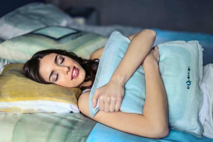 A woman lying in bed while hugging a pillow to her chest. She looks very comfortable and relaxed.