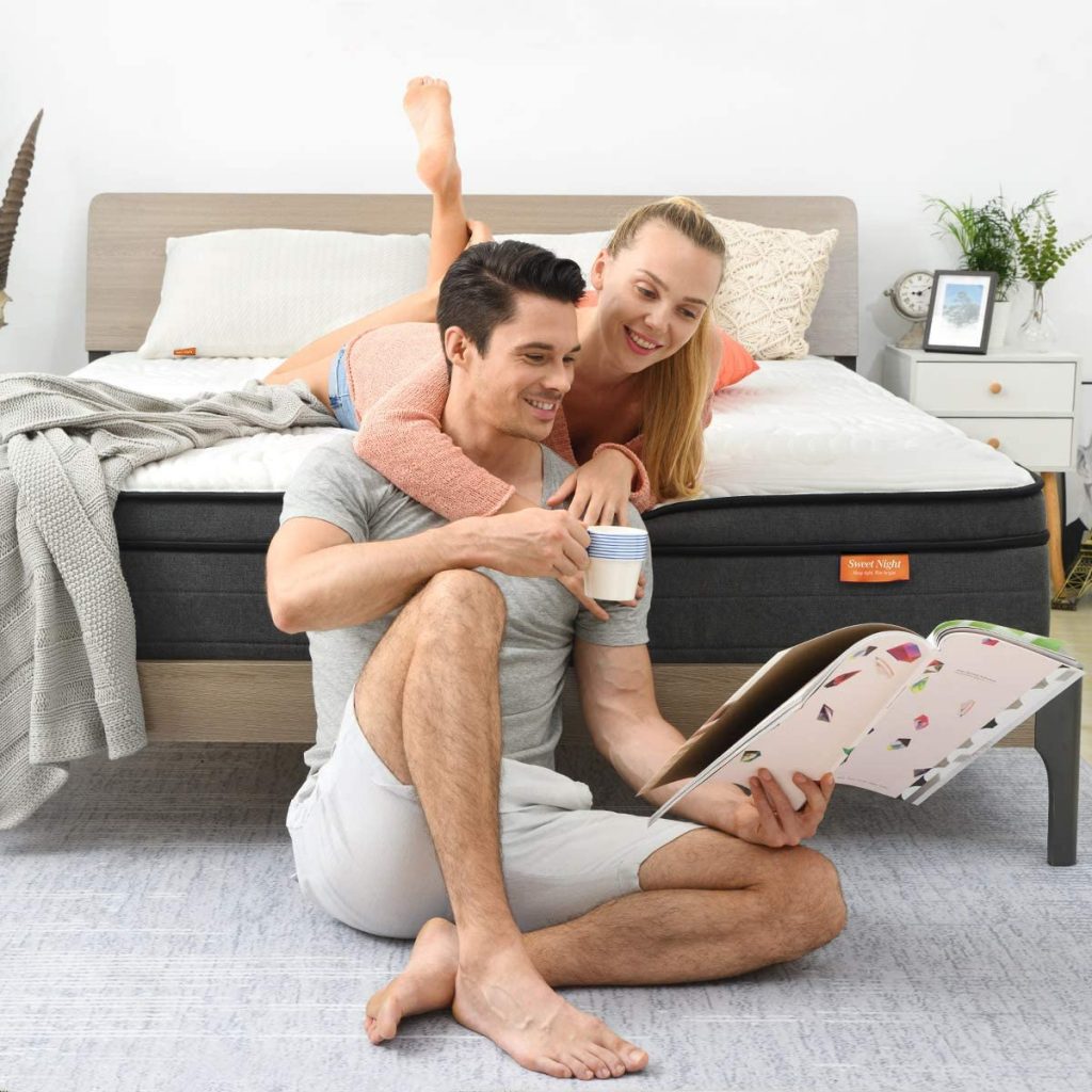 A man and a woman hanging out. The woman has her arms around the man while the man is holding a book. They are smiling.