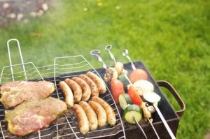 An outdoor barbecue grill sizzling with perfect and delicious food, set against a backdrop of summer skies and lush greenery