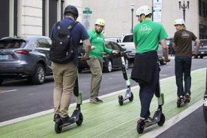 Four men wear their helmet while riding their electric scooters together outdoor. 