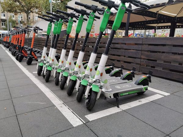 Green and white, orange scooters with stand are parked nicely and organized and viewed in the street.