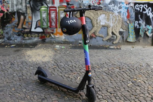 A cute and small multi color scooter is parked at the street with helmet encouraging the safety of the people when doing rides. 