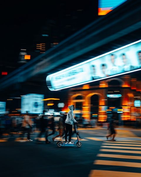 A person in a hoodie riding scooter at night.