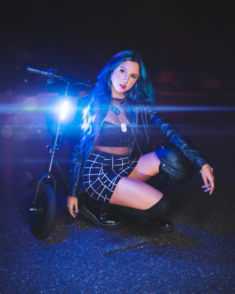 A sexy girl with blue hair wearing a checkered skirt is posing like a model on her new scooter with full brightness.