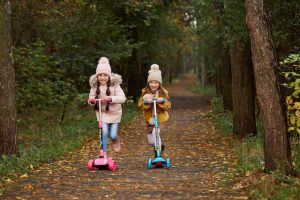 Two kids with their scooters in the forest.