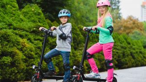 A joyful boy and girl standing confidently on their scooters, wearing helmets and radiating happiness during their adventure.