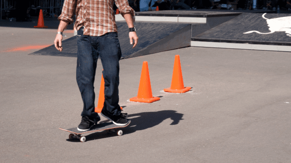 A man in a checkered shirt rides his skateboard outdoors on a bright day. 