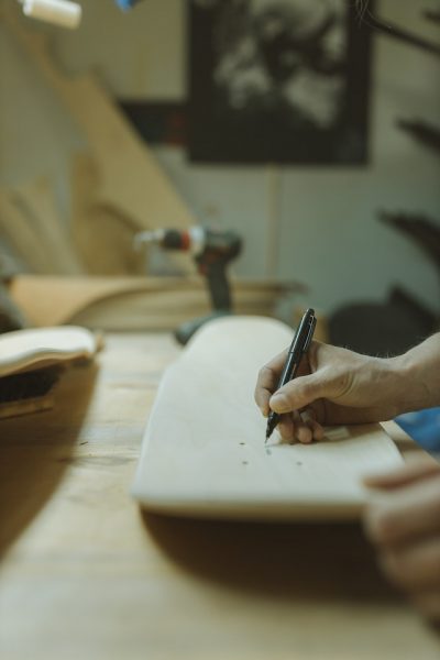 Skateboard making: Man measuring the skateboard inside the room and making sure the skateboard is shaped correctly. 