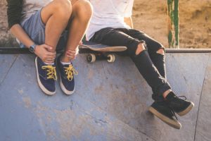 skaters are on skate ramp sitting with their skateboard showing their skateboard shoes to other skaters.