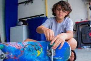 Young skateboarder fixing the wheels of skateboard at home