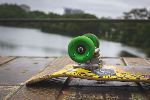 A skateboard with green wheels positioned upside down on an area near the lake. 