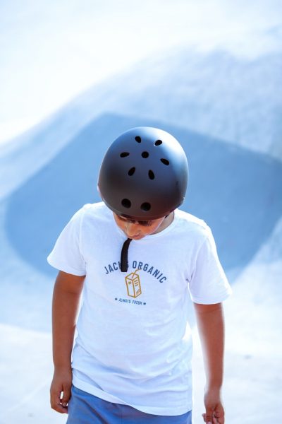 Young rider in a black headgear standing at the park.